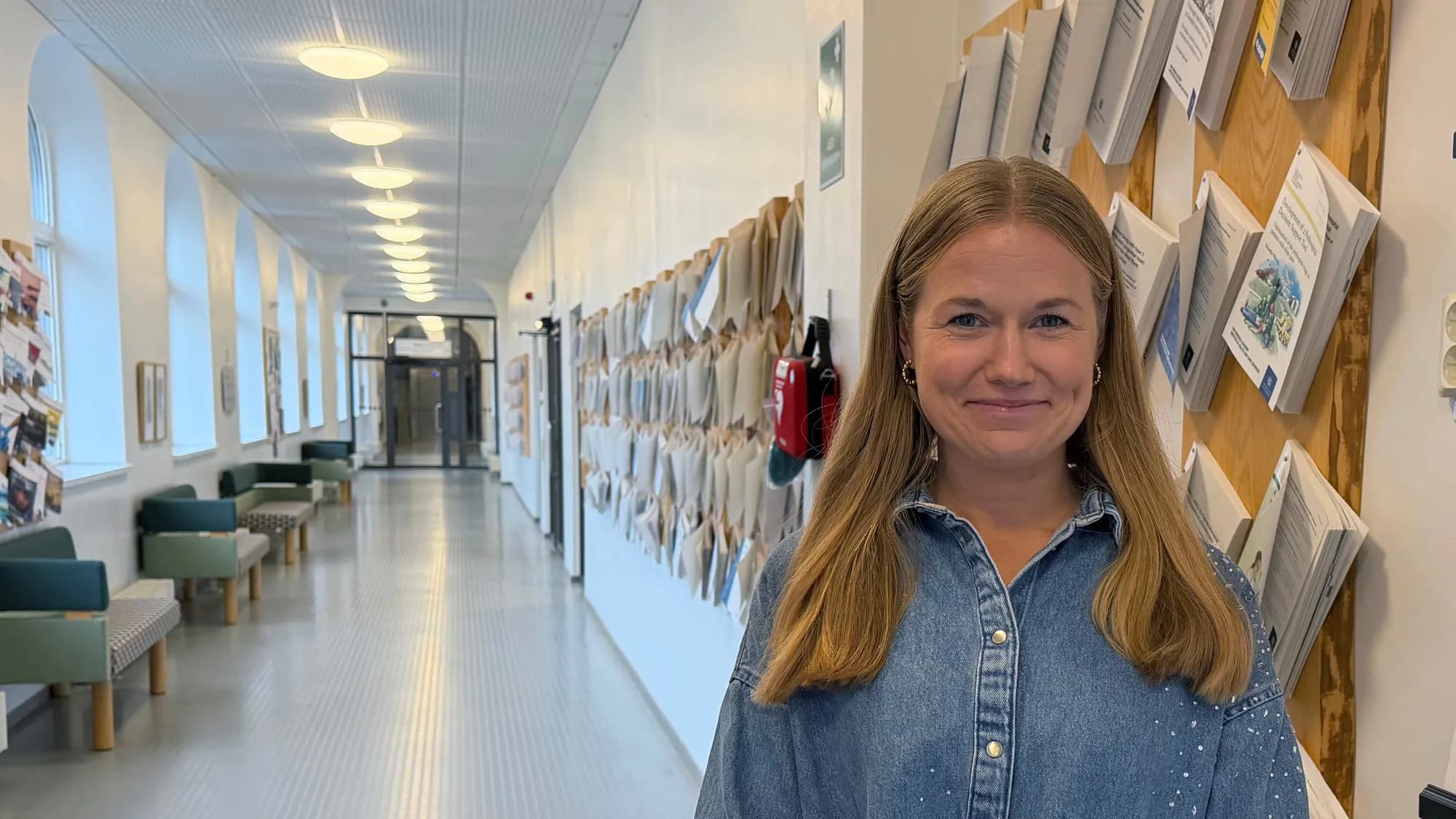 Nina Malmström står i en ljus korridor med forskningsrapporter uppsatta på väggen bakom sig.